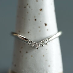 A white gold and diamond V shaped shadow style wedding band on a white ceramic display on a blue grey background