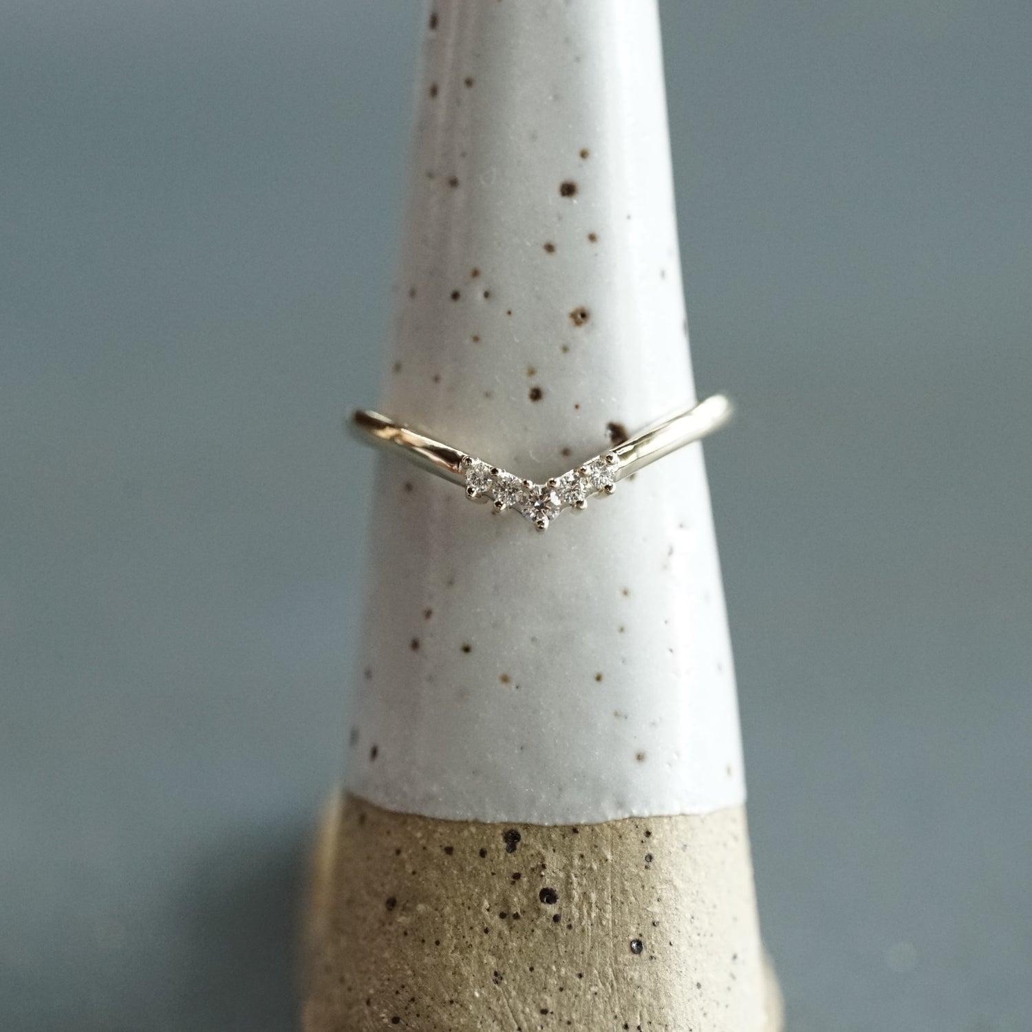 A yellow gold and diamond V shaped shadow style wedding band on a white ceramic display with a blue grey background