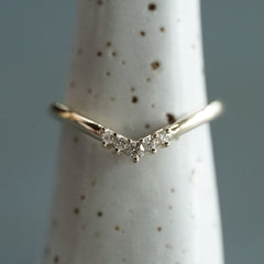 A yellow gold and diamond V shaped shadow style wedding band on a white ceramic display on a blue grey background