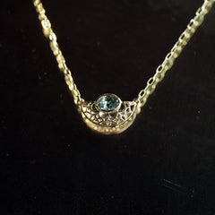 A yellow gold and bezel seat seafoam color sapphire on a light open link chain hanging in front of black mirrored background
