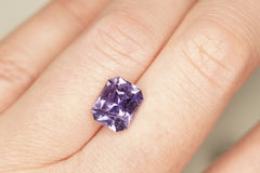Purple gemstone on a finger against a neutral background
