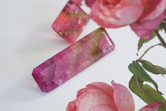 Pink and green gemstones on a white surface with pink flowers in the background