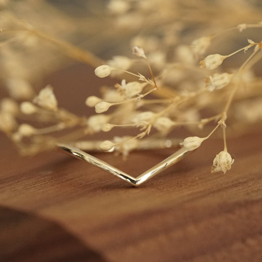 a 14K yellow gold shadow style band rests on a wood display with white flowers