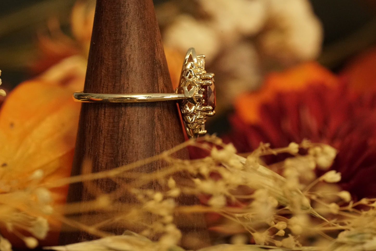 a magnificent 18K yellow gold ring with an oval chocolate zircon center stone surrounded by round and pear shape diamonds which color fade from brown to white in a floral halo shown on a wood display in warm fall foliage