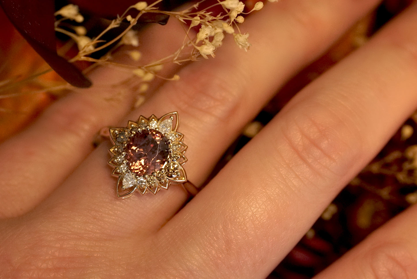 a magnificent 18K yellow gold ring with an oval chocolate zircon center stone surrounded by round and pear shape diamonds which color fade from brown to white in a floral halo shown on a light skinned left hand