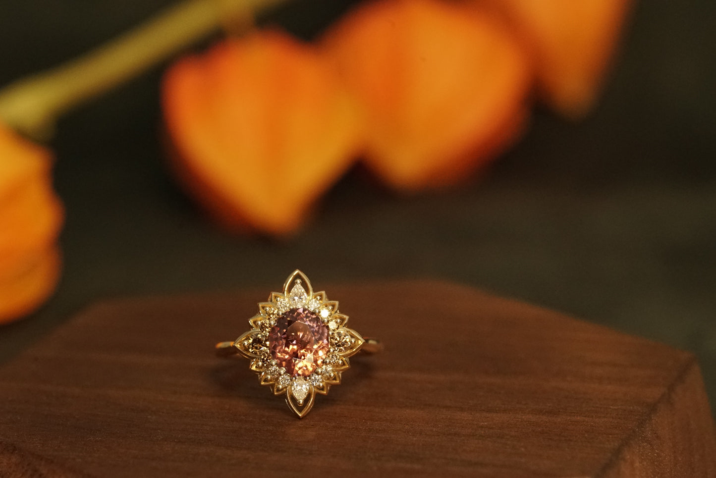 a magnificent 18K yellow gold ring with an oval chocolate zircon center stone surrounded by round and pear shape diamonds which color fade from brown to white in a floral halo shown on a wood display