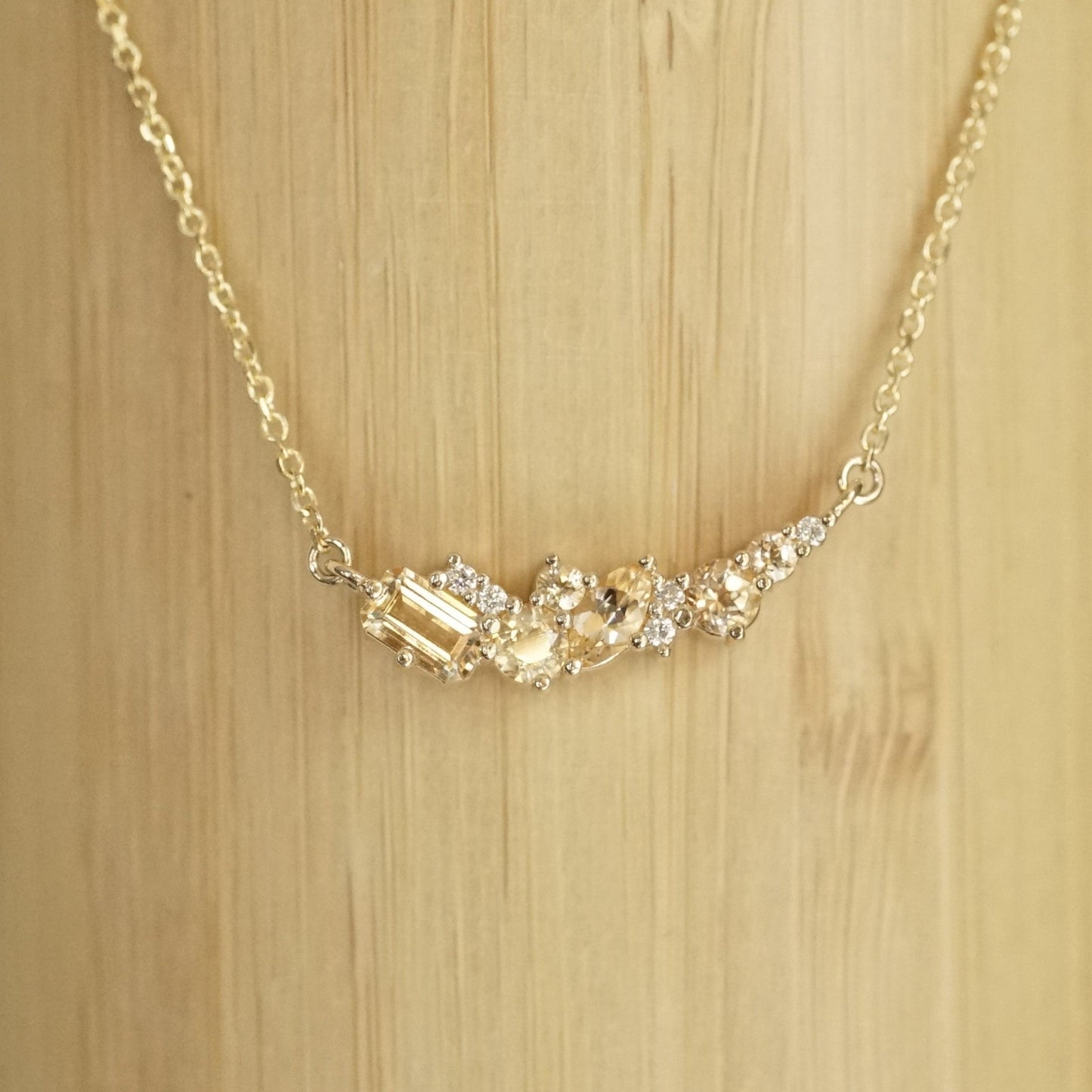 golden topaz of various sizes and shapes are mixed with round white diamonds in a pendant and suspended on an open link yellow gold chain in front of a bamboo background