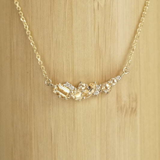 golden topaz of various sizes and shapes are mixed with round white diamonds in a pendant and suspended on an open link yellow gold chain in front of a bamboo background