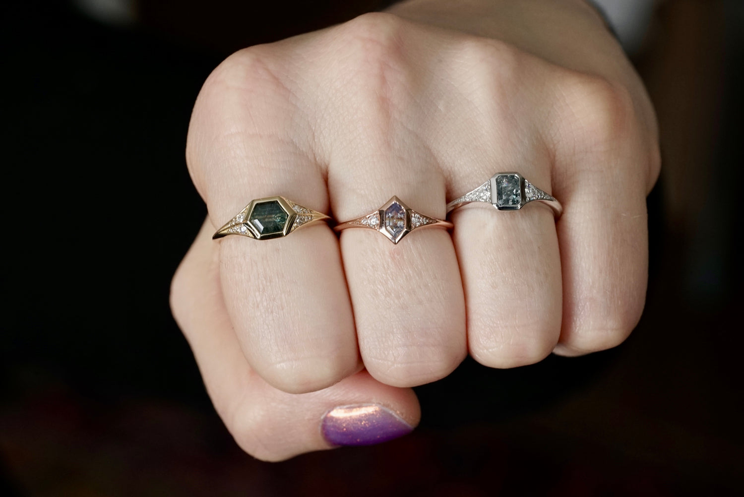 Close-up of a hand wearing three rings with gemstones on a dark background