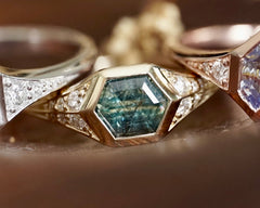 Close-up of a gold ring with a blue gemstone and diamond accents on a blurred background.