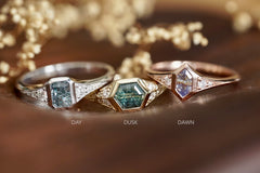 Three sapphire and diamond rings in 14k gold on a wooden surface with flowers in the background