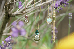 Three gold necklaces with gemstone pendants hanging among lavender flowers.