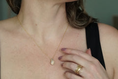 Close-up of a person wearing a gold necklace with a teardrop pendant and multiple gold rings on a neutral background.