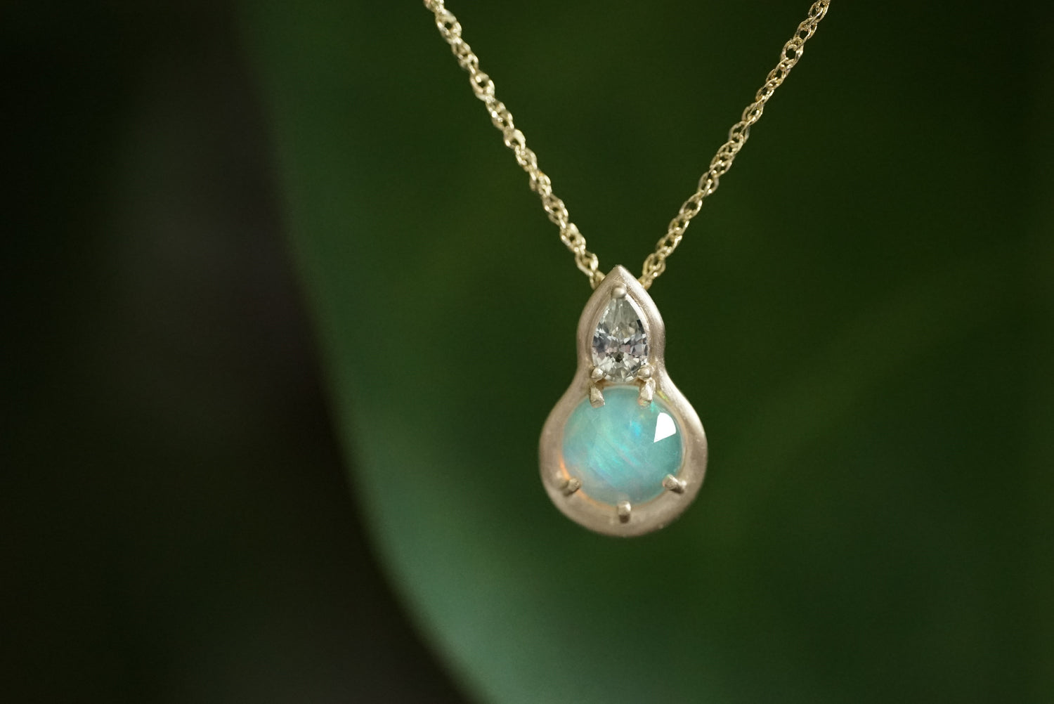 Teardrop-shaped pendant with a green sapphire and opal and gold chain on a dark background