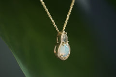 Gold necklace with a teardrop-shaped pendant featuring a green sapphire and opal gemstone on a dark background