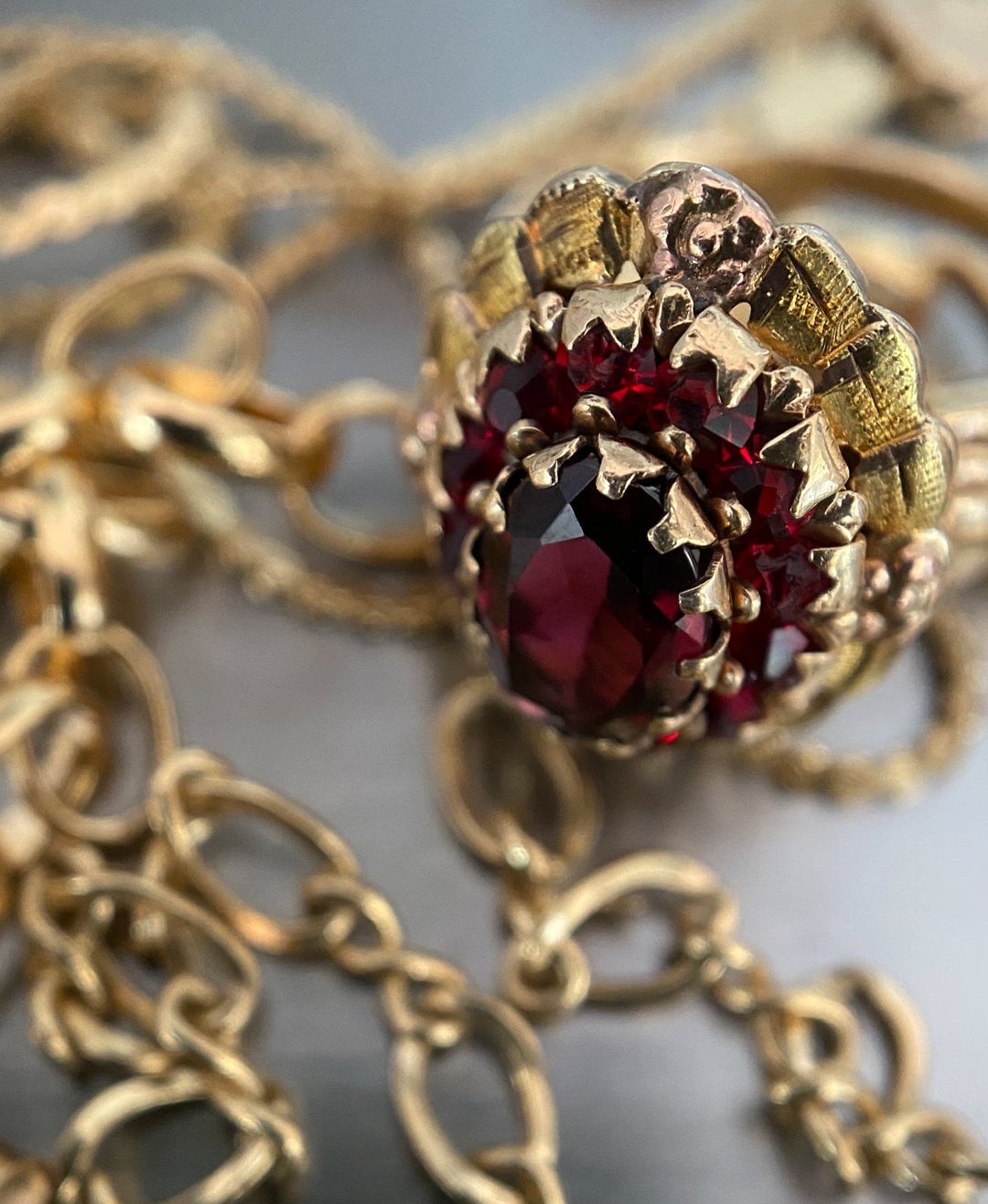 a mix of yellow gold chains lays under a yellow gold and garnet ring on a stainless steel table