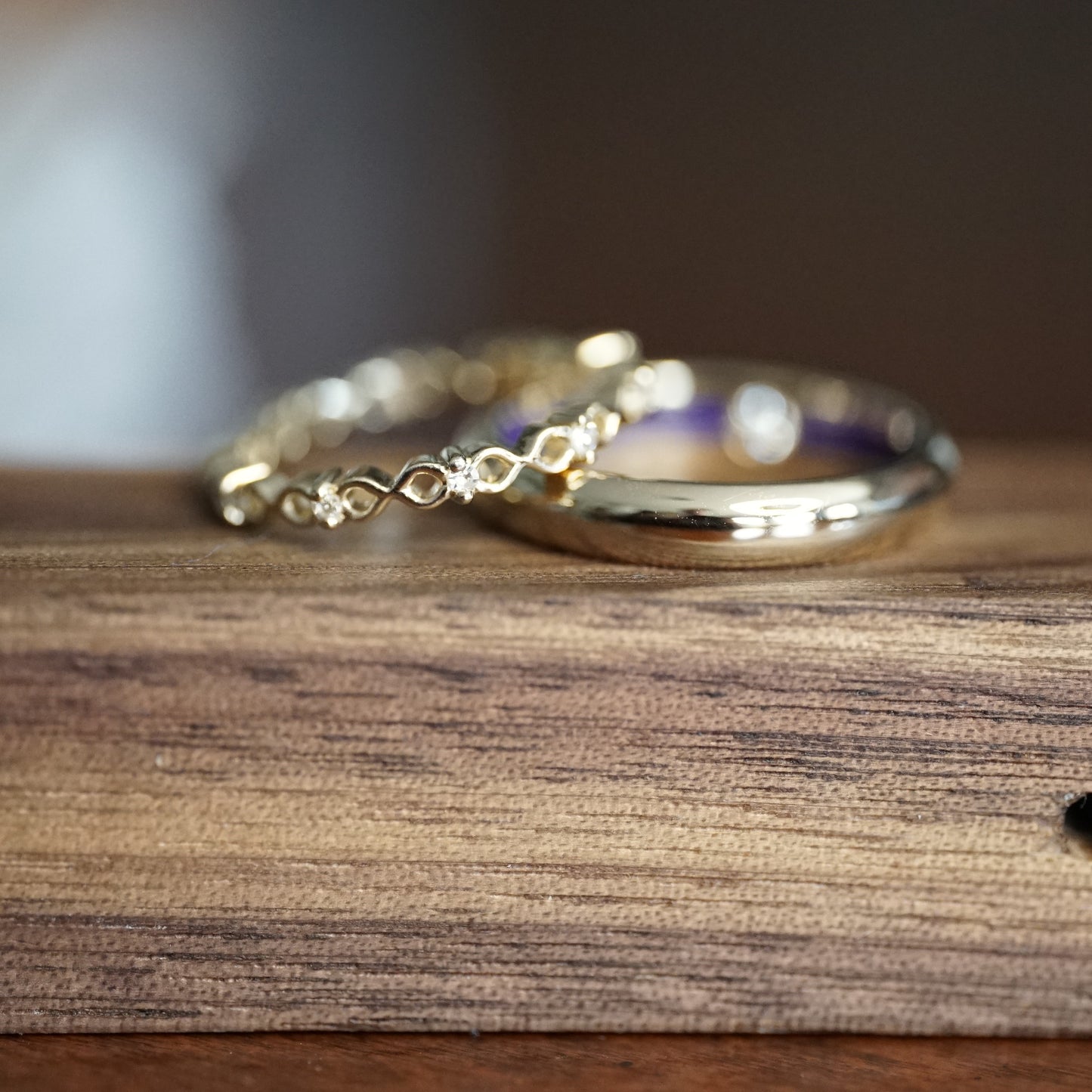 a pair of yellow gold wedding bands, one with 10 diamond accents on a wooden display