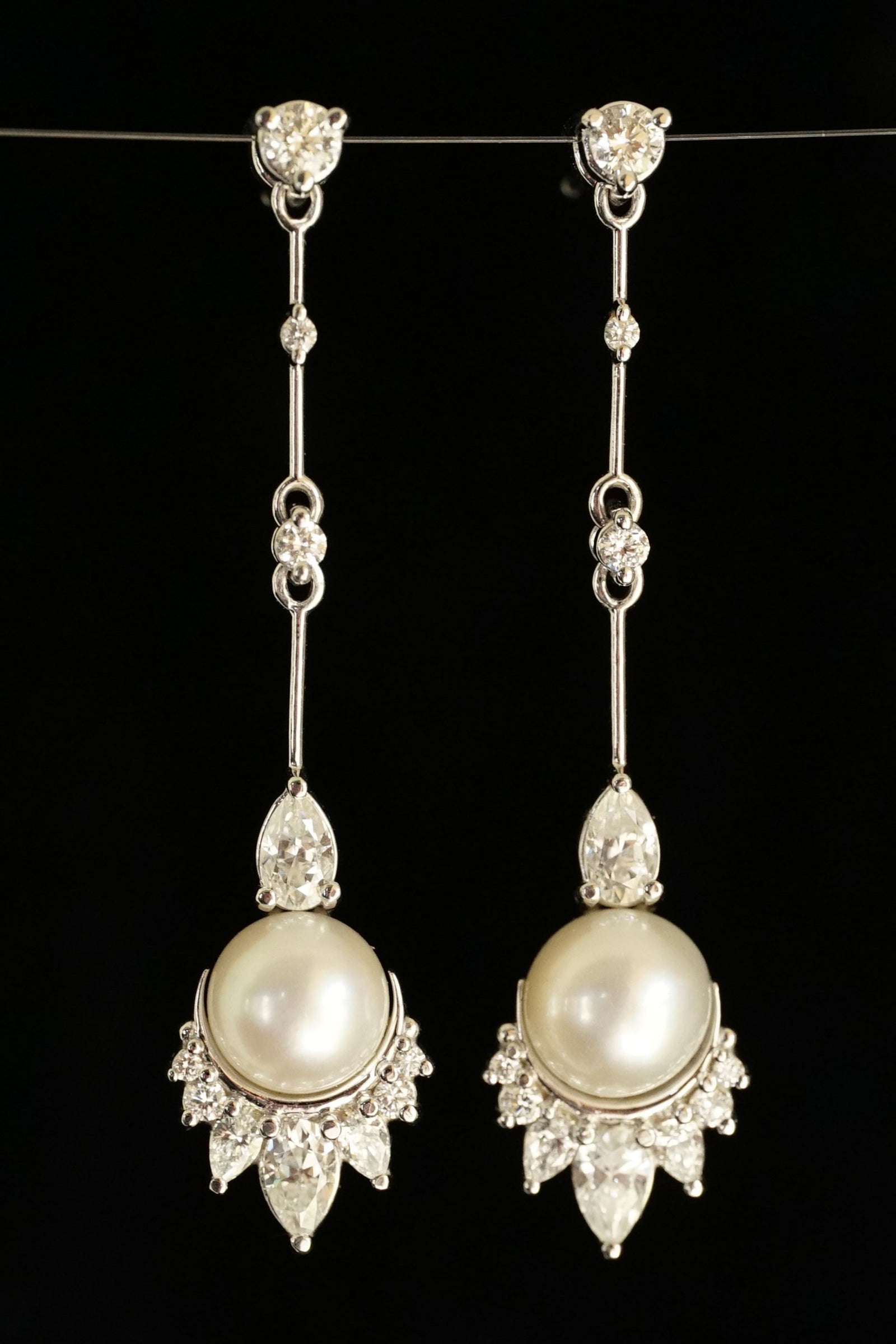 a pair of white gold pearl and diamond drop earrings on a black backdrop