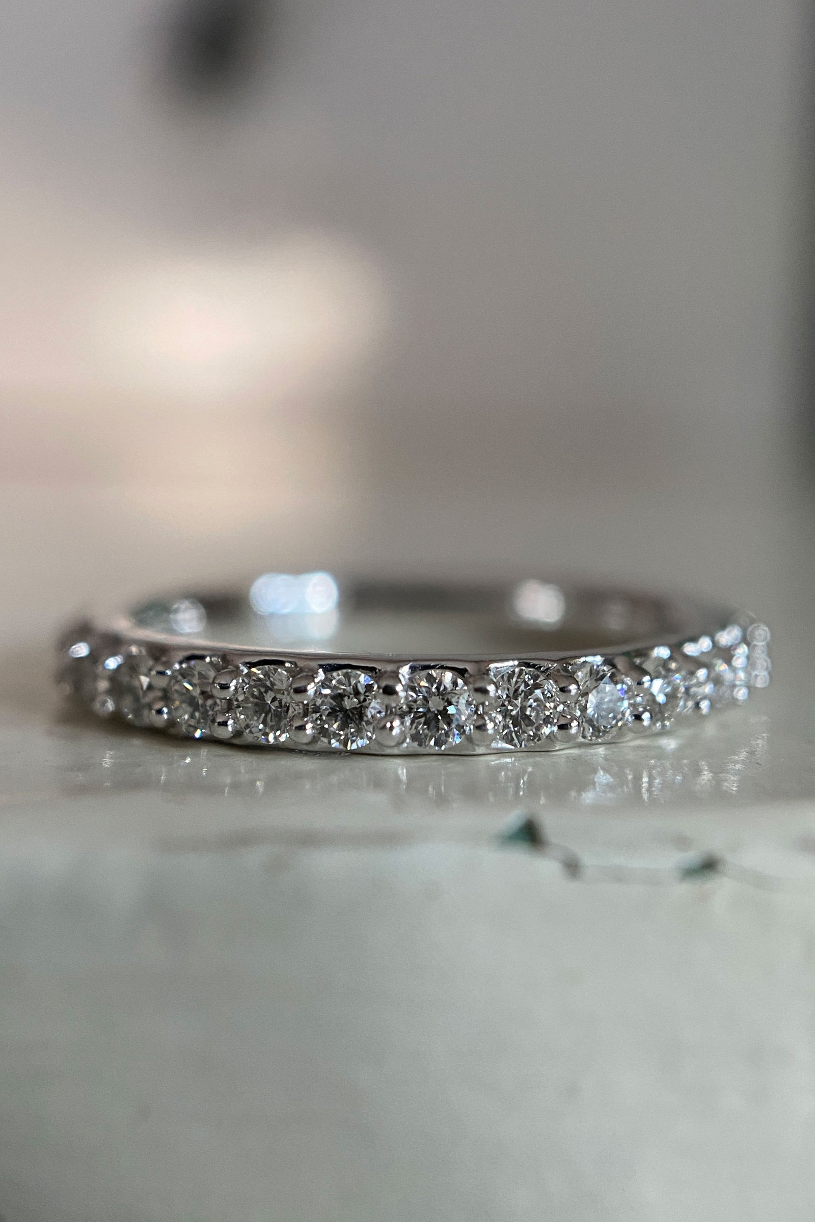 a white gold and diamond wedding band on a shiny white surface