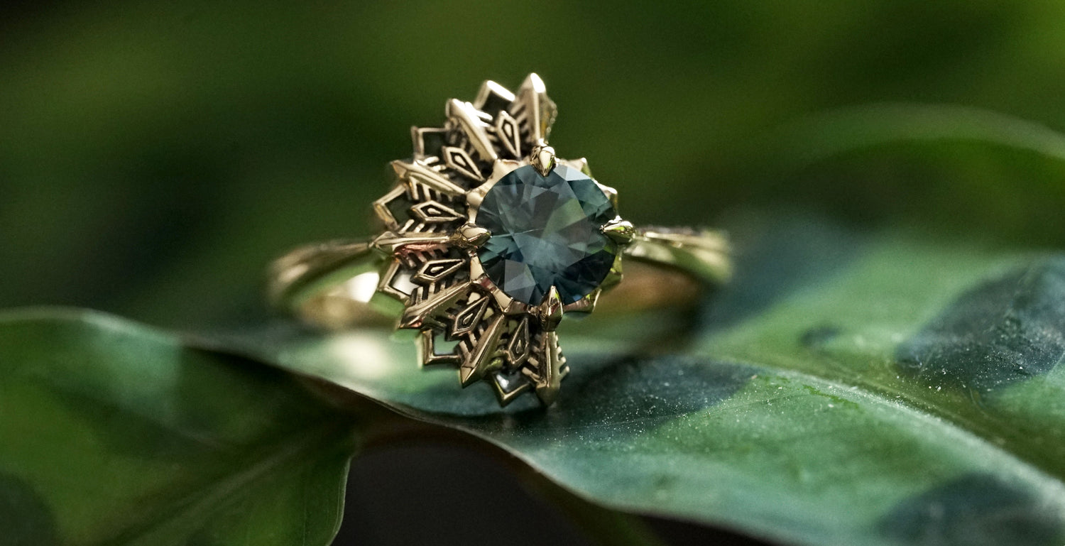14K yellow gold ring with a deep teal sapphire on a green leaf