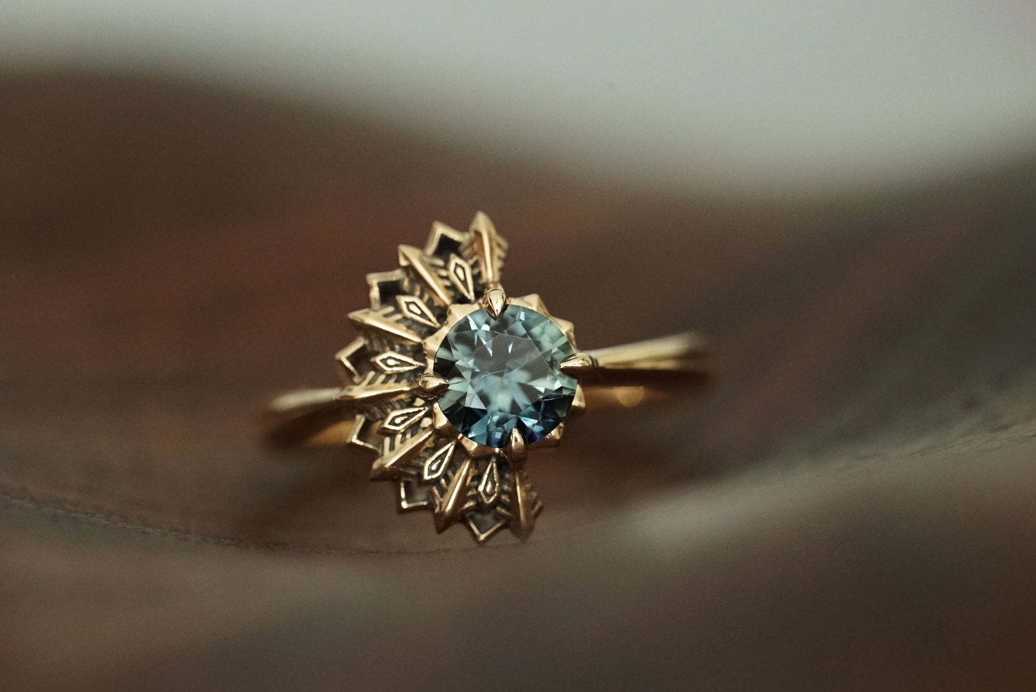 14K yellow gold ring with a deep teal sapphire on a soft brown background