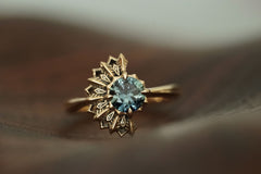 14K yellow gold ring with a deep teal sapphire on a soft brown background