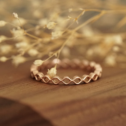 a rose gold ring rests on a wood base with white flowers