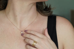 Close-up of a person wearing a delicate necklace with a small pendant, hand with rings, and blurred background.