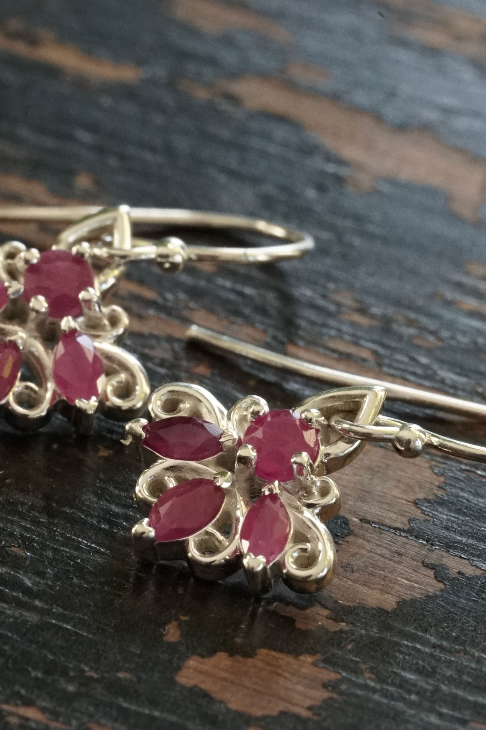 a pair of silver and ruby drop earrings on an antiqued wood base