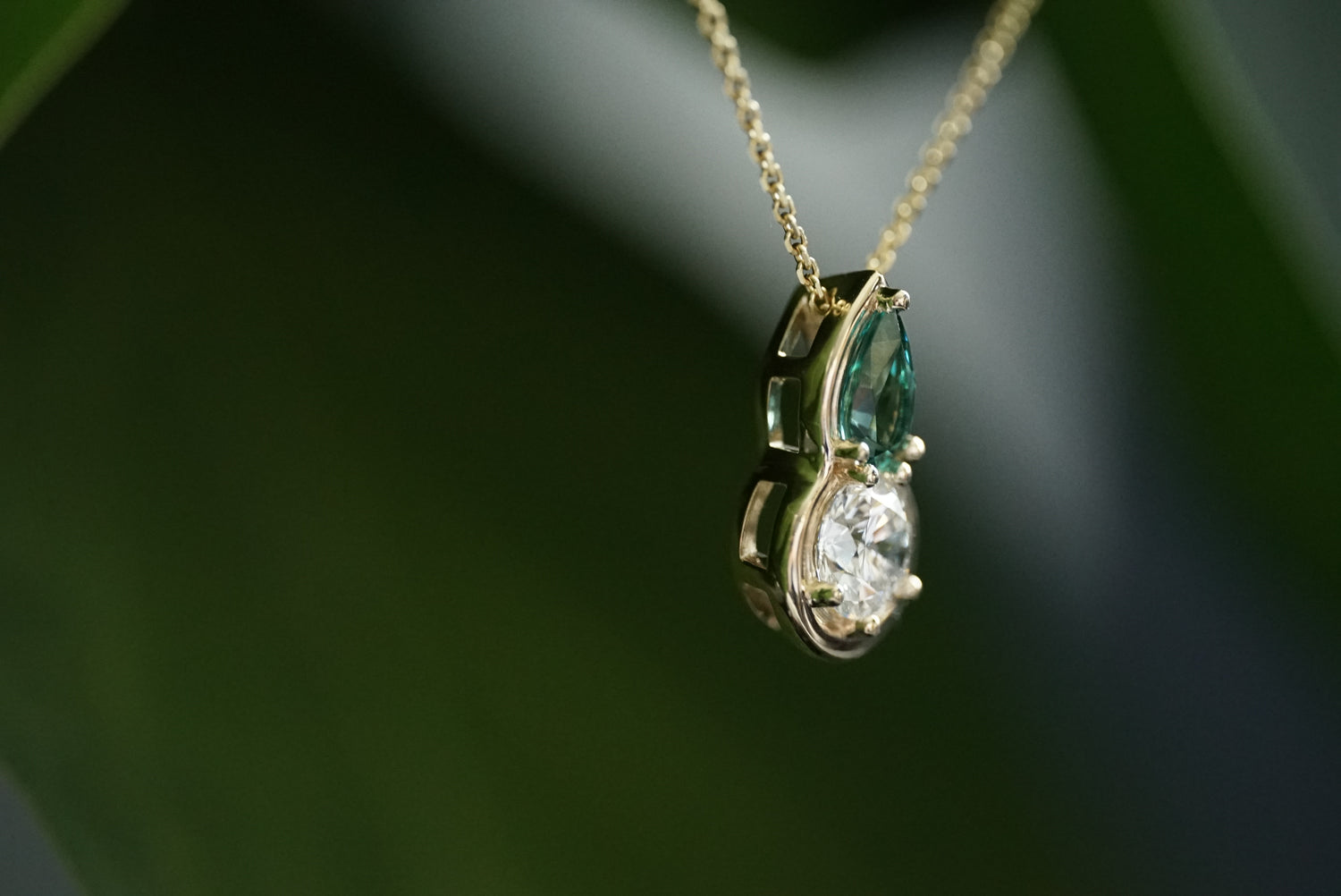 Gold necklace with a pendant featuring a tourmaline and diamond on a dark background