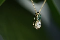 Gold necklace with a pendant featuring a tourmaline and diamond on a dark background