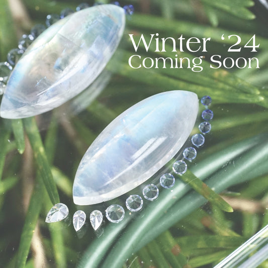 a teaser photo of a pair of moonstones shown with diamonds and ombre sapphires in front of green foliage