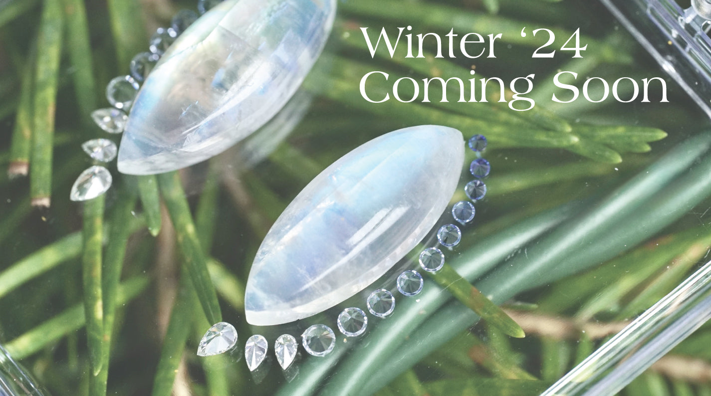 a teaser photo of a pair of moonstones shown with diamonds and ombre sapphires in front of green foliage