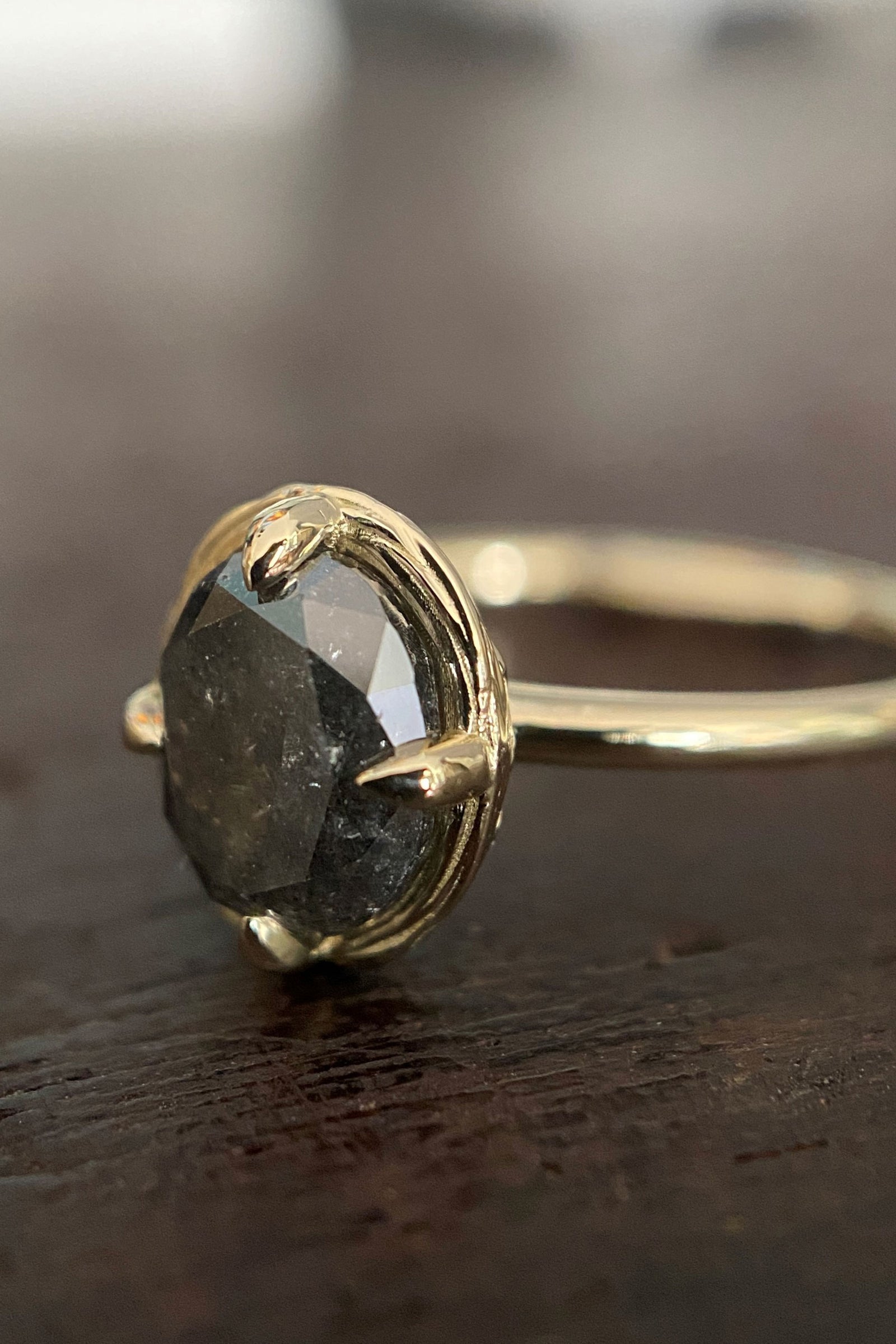 a yellow gold and black diamond engagement ring on a dark wood base