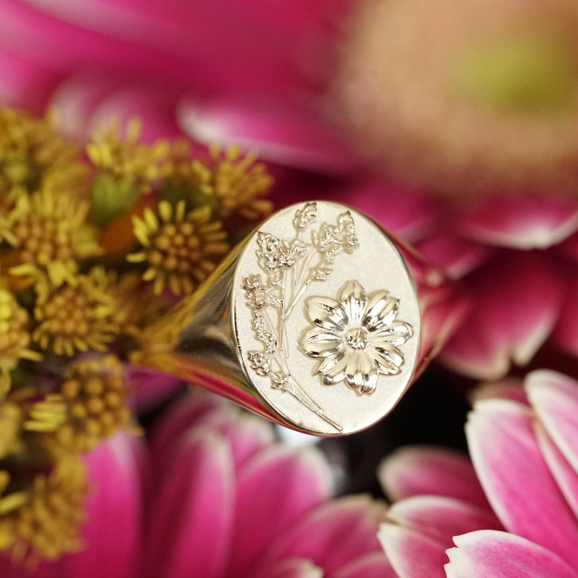 a macro photo of a yellow gold signet rings with floral motifs resting on pink and yellow flowers