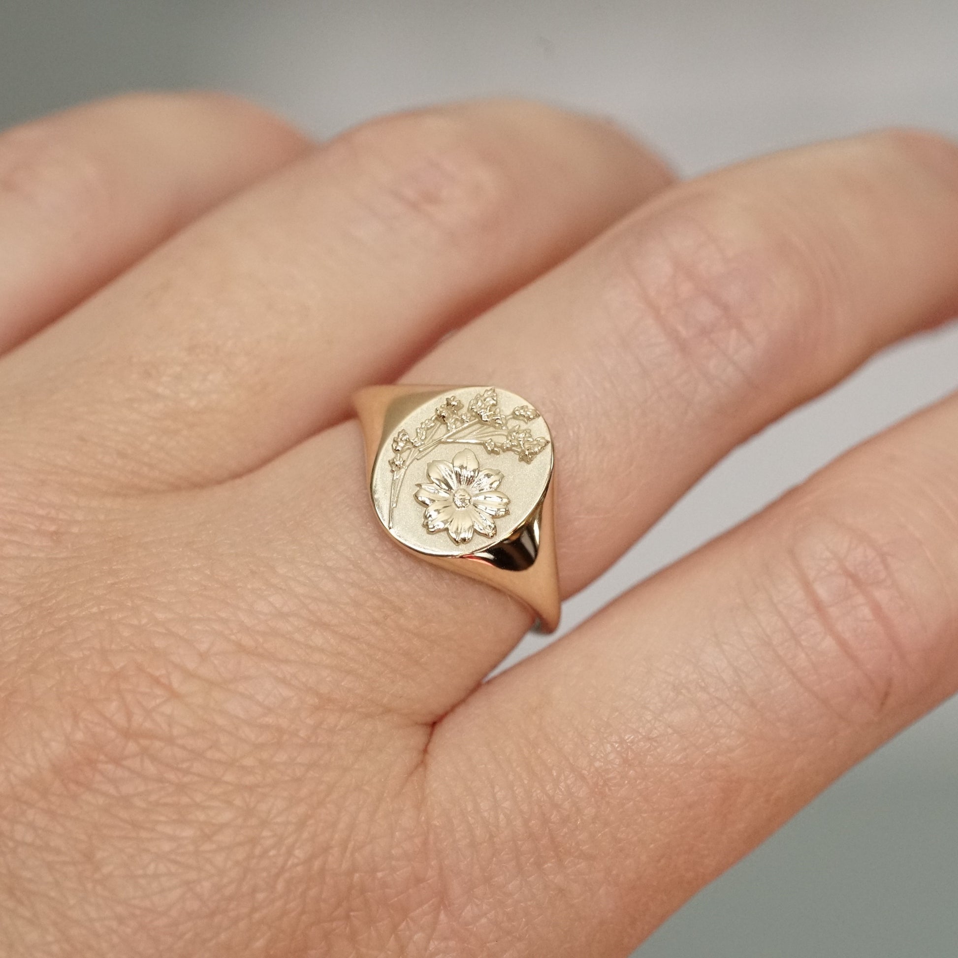 a yellow gold signet ring carved with floral motifs on a light skinned left hand