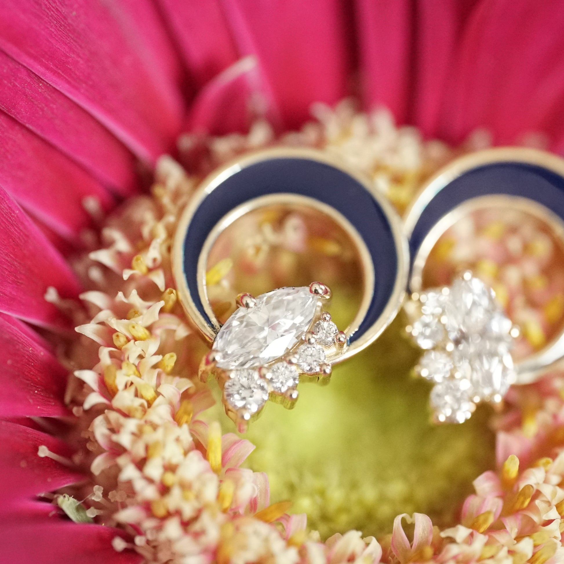 a pair of diamond button earrings with one large marquise and 4 small round diamonds at the base of a crescent shape element filled with blue enamel resting on a pink and yellow flower