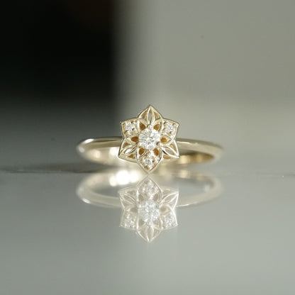 a yellow gold ring with an open wirework flower inspired by daffodils with a single diamond prong set center stone and 3 prong set diamond accents in the petals on a reflective background