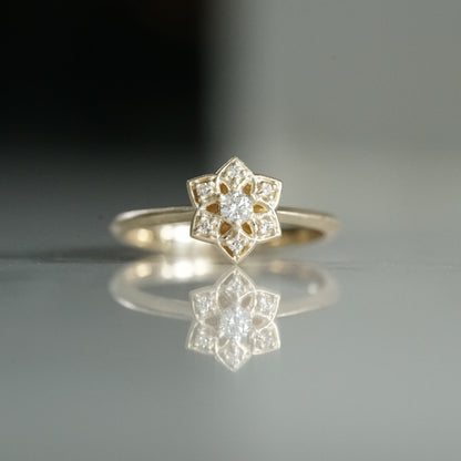 a yellow gold ring with an open wirework flower inspired by daffodils with a single diamond prong set center stone and 6 prong set diamond accents in the petals on a reflective background