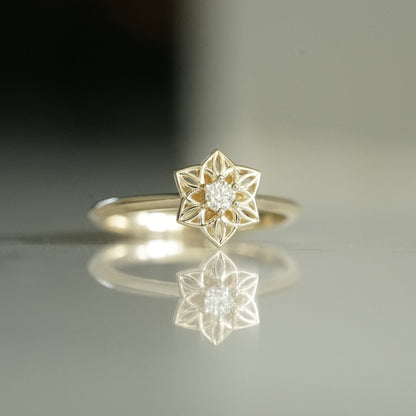 a yellow gold ring with an open wirework flower inspired by daffodils with a single diamond prong set center stone on a reflective background