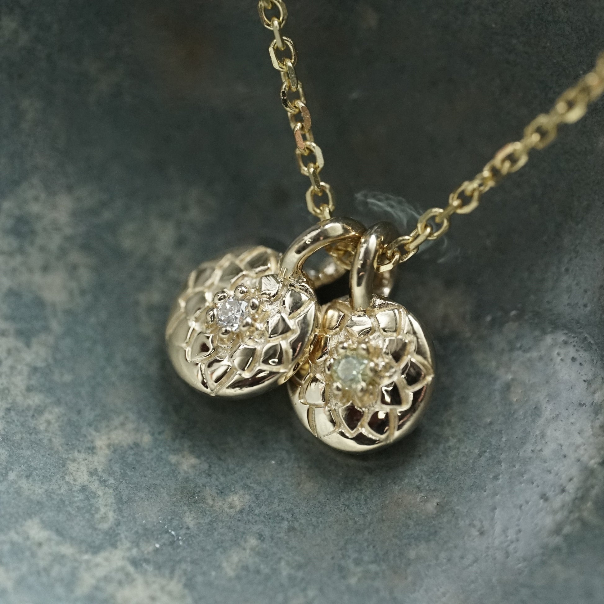 a macro photo of 14K yellow gold and diamond pendants in a blue ceramic dish