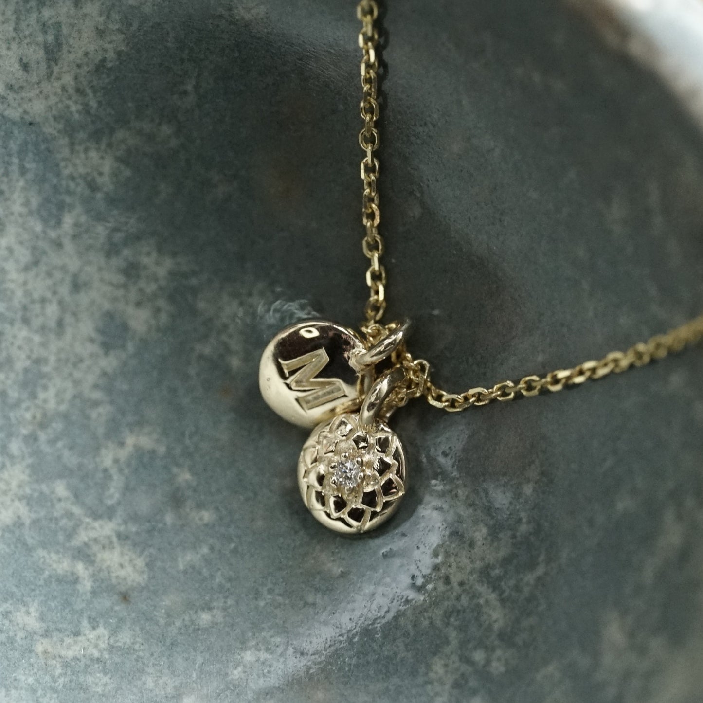 a macro photo of two 14K yellow gold and diamond pendants in a blue ceramic bowl