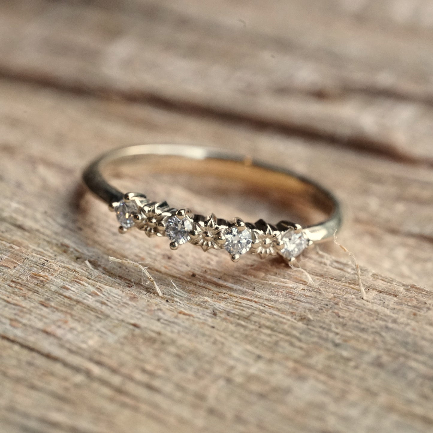 a yellow gold ring with 3 flower elements and 4 diamonds rests on a wood display