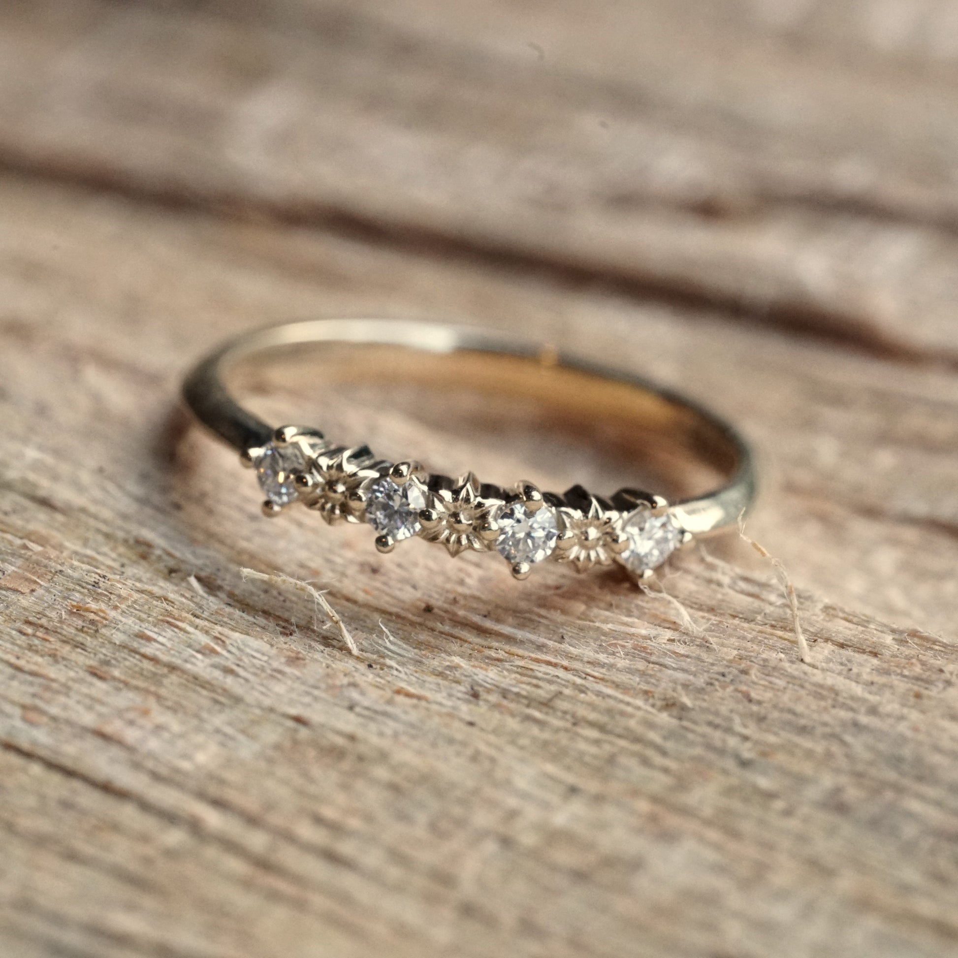 a yellow gold ring with 3 flower elements and 4 diamonds rests on a wood display