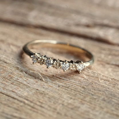 a yellow gold ring with 3 flower elements and 4 diamonds rests on a wood display