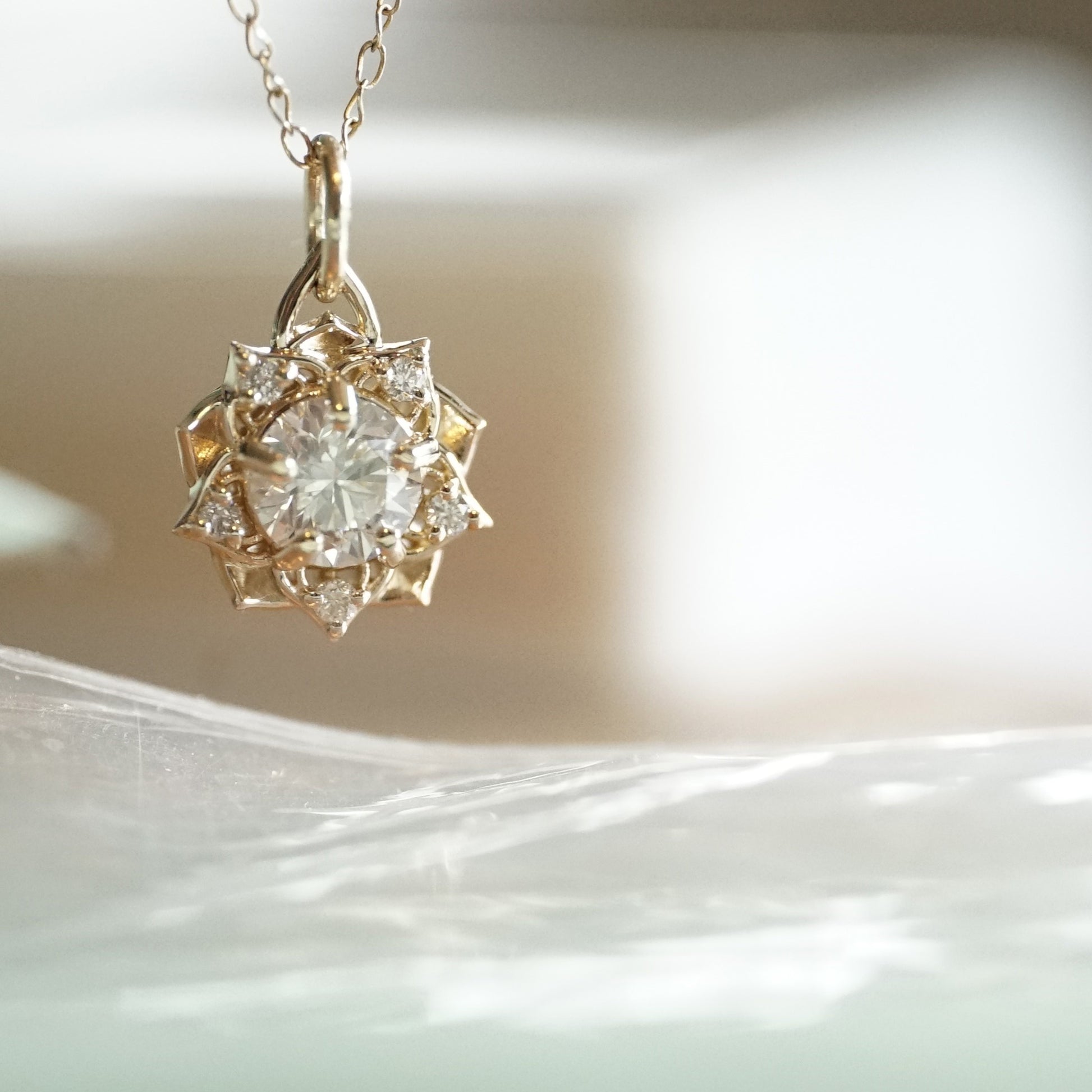 a yellow gold pendant with a large diamond center stone and 5 diamond accents in a floral design on an open link chain suspended over a reflective wavy surface