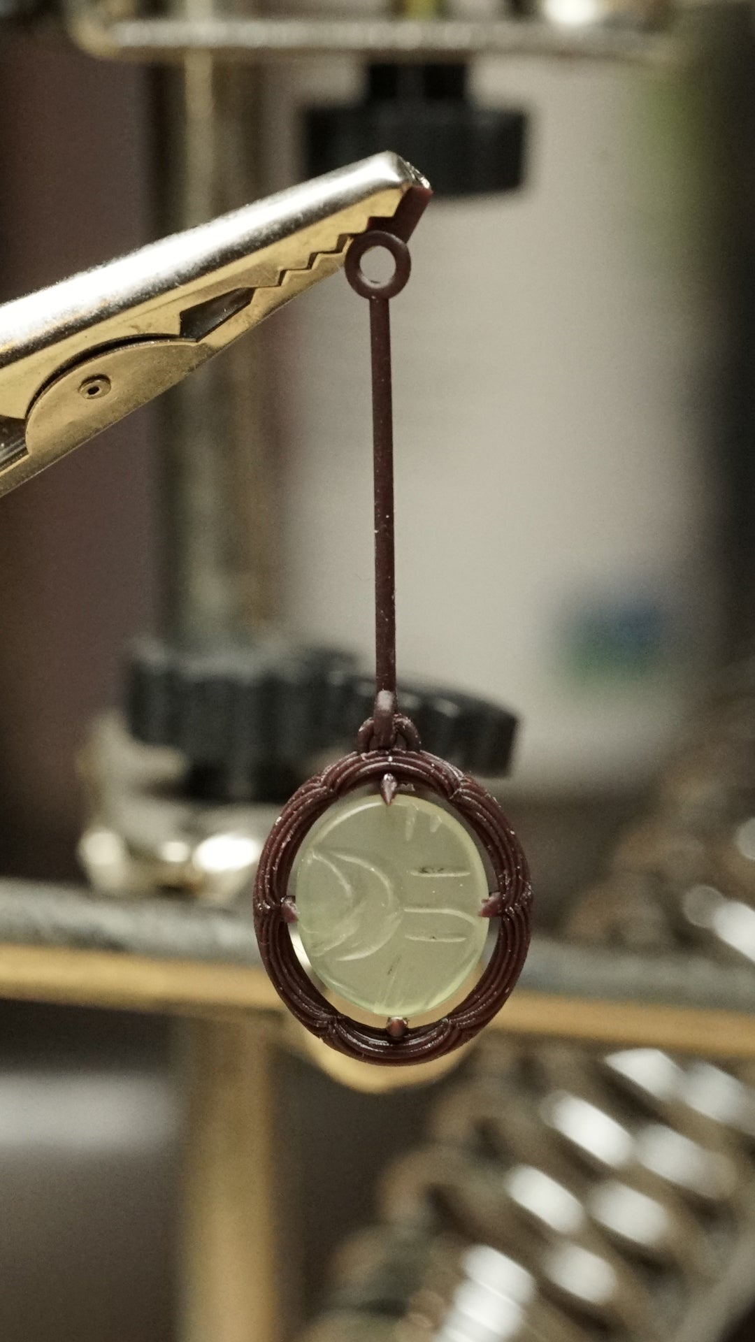 a 3d printed wax model with a custom cut jade cabochon hangs on a jewelers bench