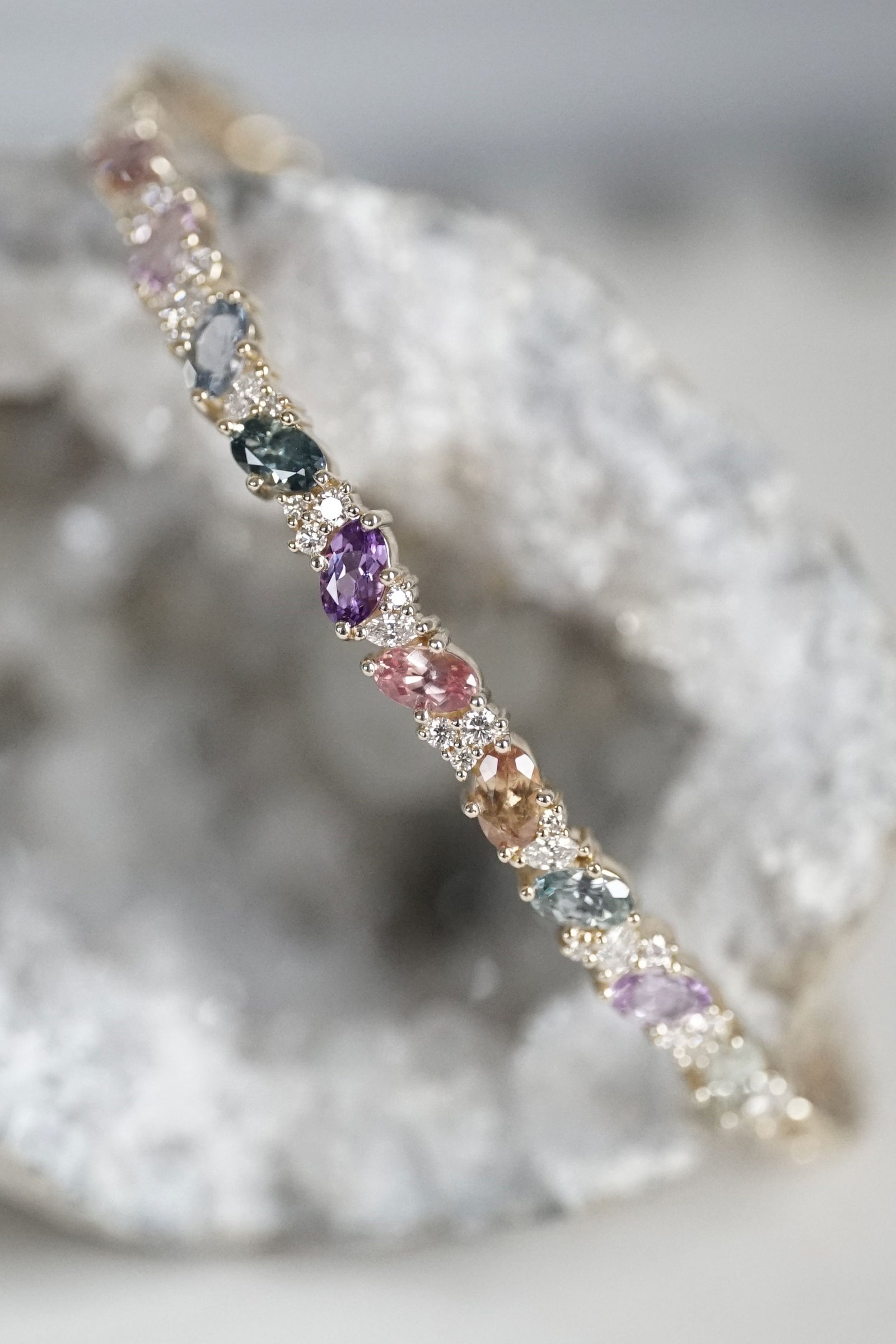 a yellow gold diamond and mulit colored sapphire bracelet on a geode