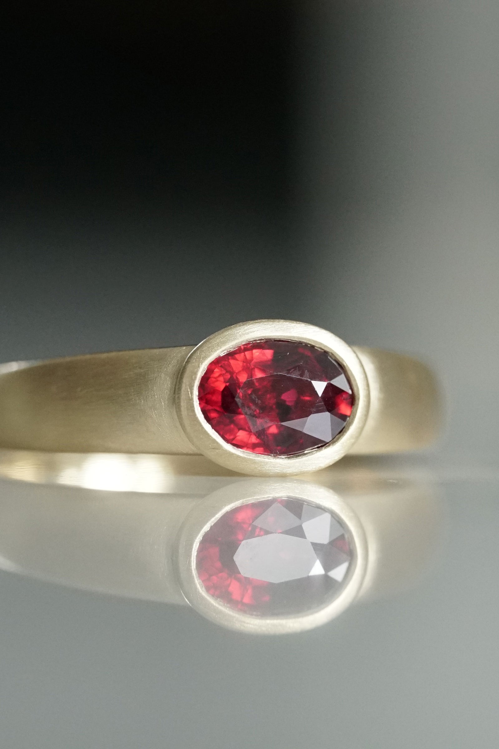 a yellow gold and ruby ring on a reflective base