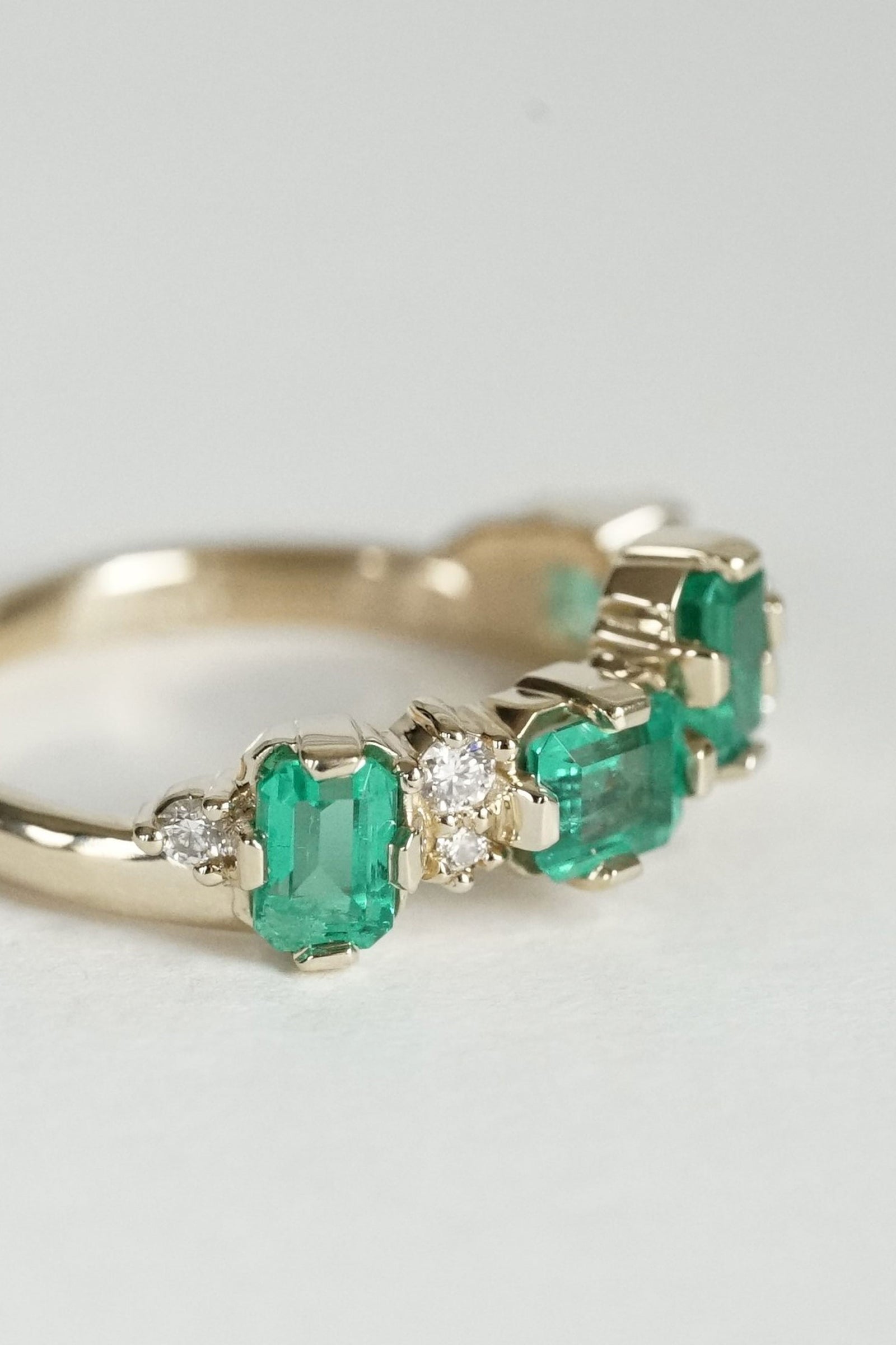a yellow gold diamond and emerald ring rests on a white groundplane